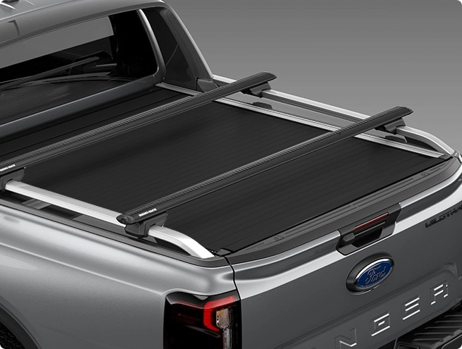 Top-down view of a grey Ford Ranger truck bed with a black roll-up tonneau cover and two black roof rack crossbars.