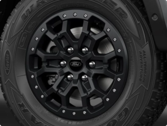 Close-up of a black multi-spoke wheel on a Ford Ranger, with "Kevlar" and "ALL-TERRAIN ADVENTURE" tire lettering visible.