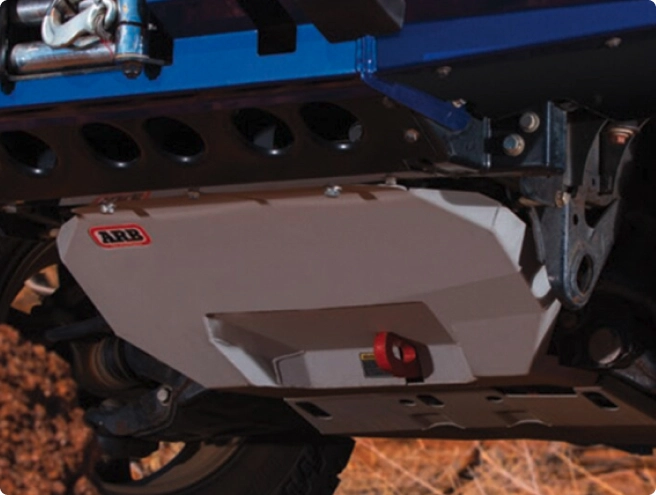 Undercarriage view of a vehicle showing a light grey ARB skid plate with a red recovery point.