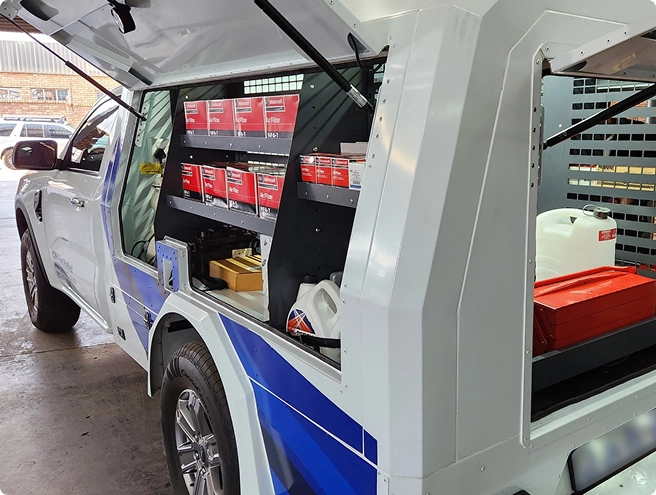 A white utility truck with blue and white graphics, showing its open compartments filled with shelves, red boxes, and containers.