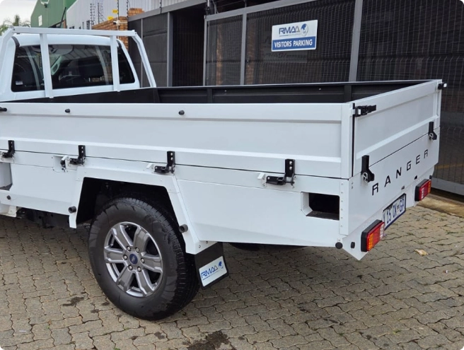 A white Ford Ranger pickup truck with a white flatbed utility tray, featuring "RANGER" text on the back, is parked on a paved surface.