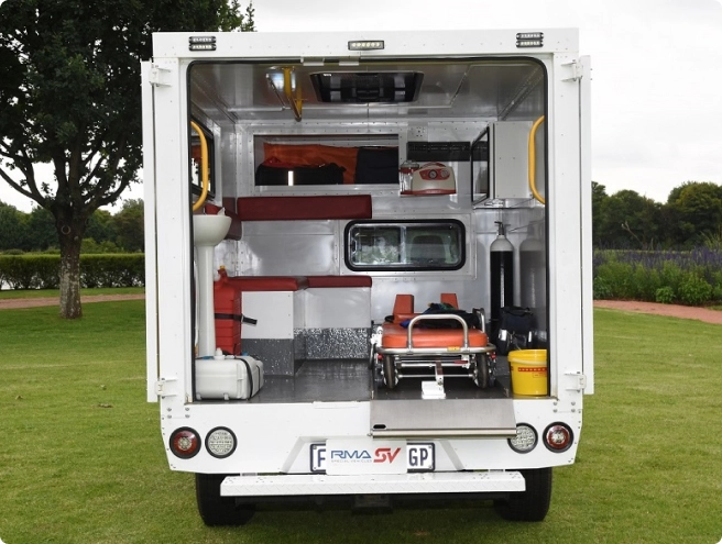 The rear view of a white ambulance, revealing its interior with a stretcher, oxygen tank, sink, and other medical equipment.
