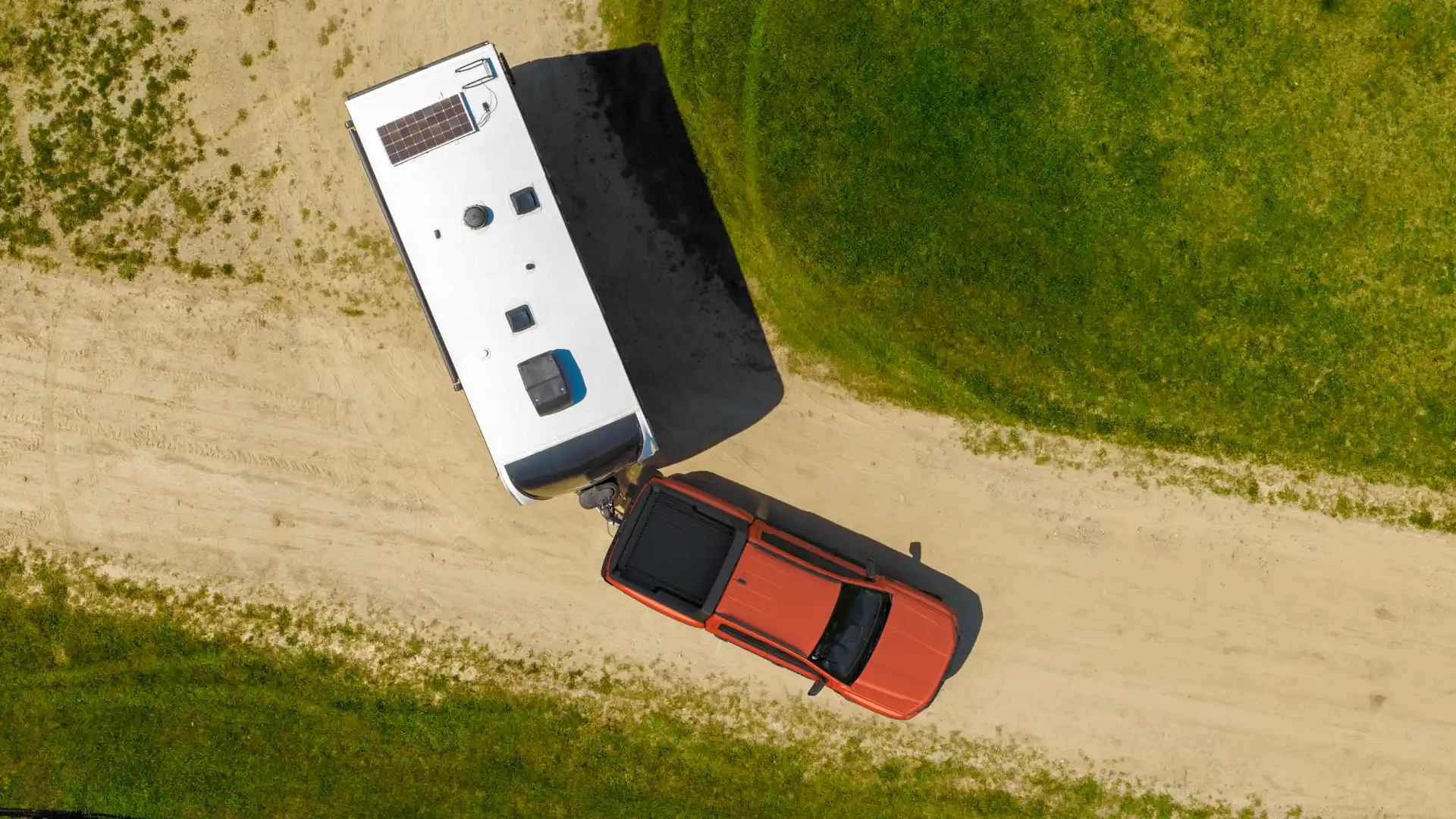 Ford Ranger towing caravan on dirt road top view.
