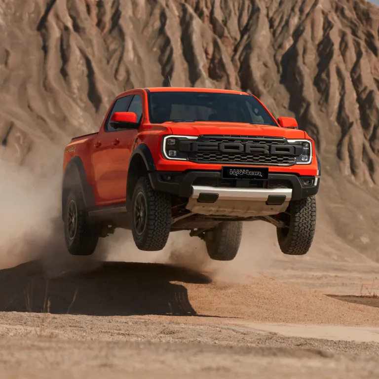 Red pickup truck with dirt bike loaded in rear with two people outdoors.