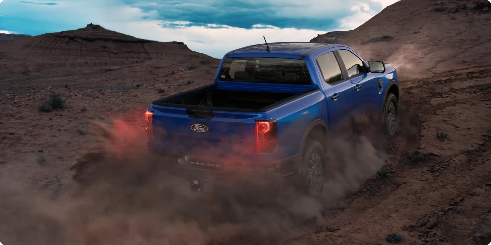 Blue pickup truck driving off road kicking up dust.