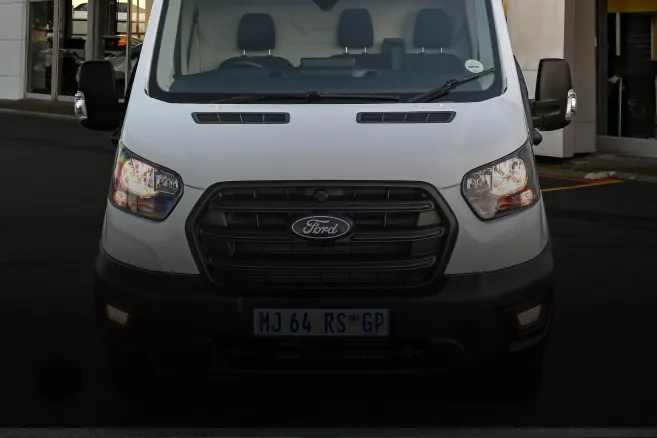 Front view of white Ford Transit van with headlights on